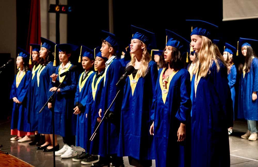 A group of graduates are singing into microphones on a stage.