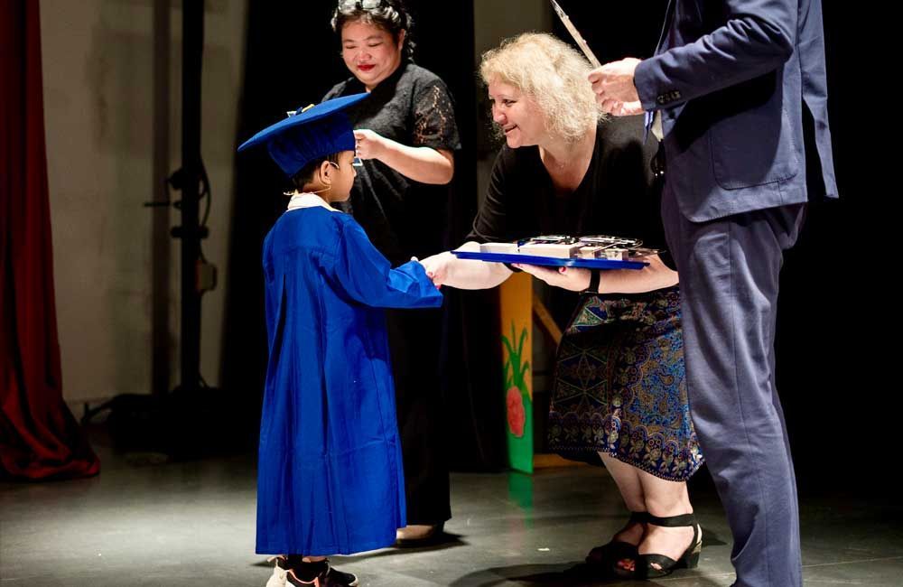 A little girl in a graduation cap and gown is shaking hands with a woman.