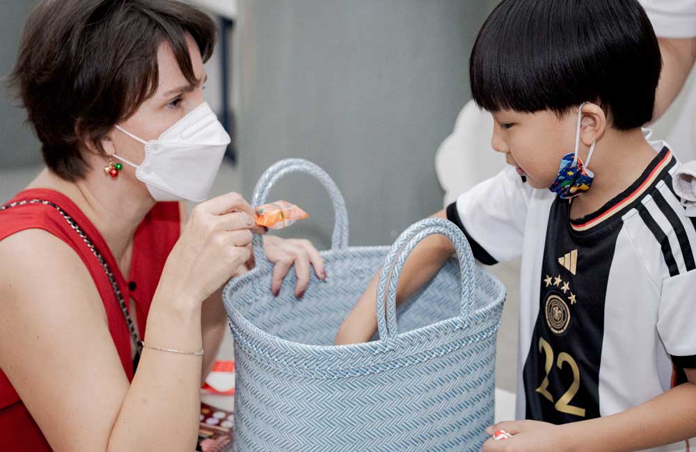 A woman wearing a mask is feeding a child from a basket.