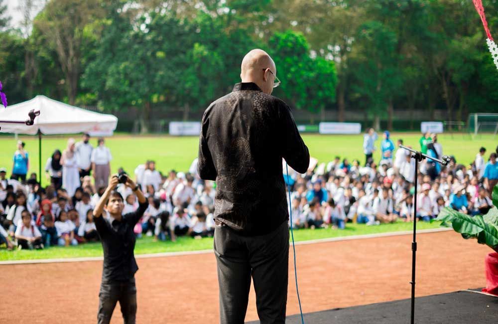 A man is standing in front of a microphone in front of a crowd of people.