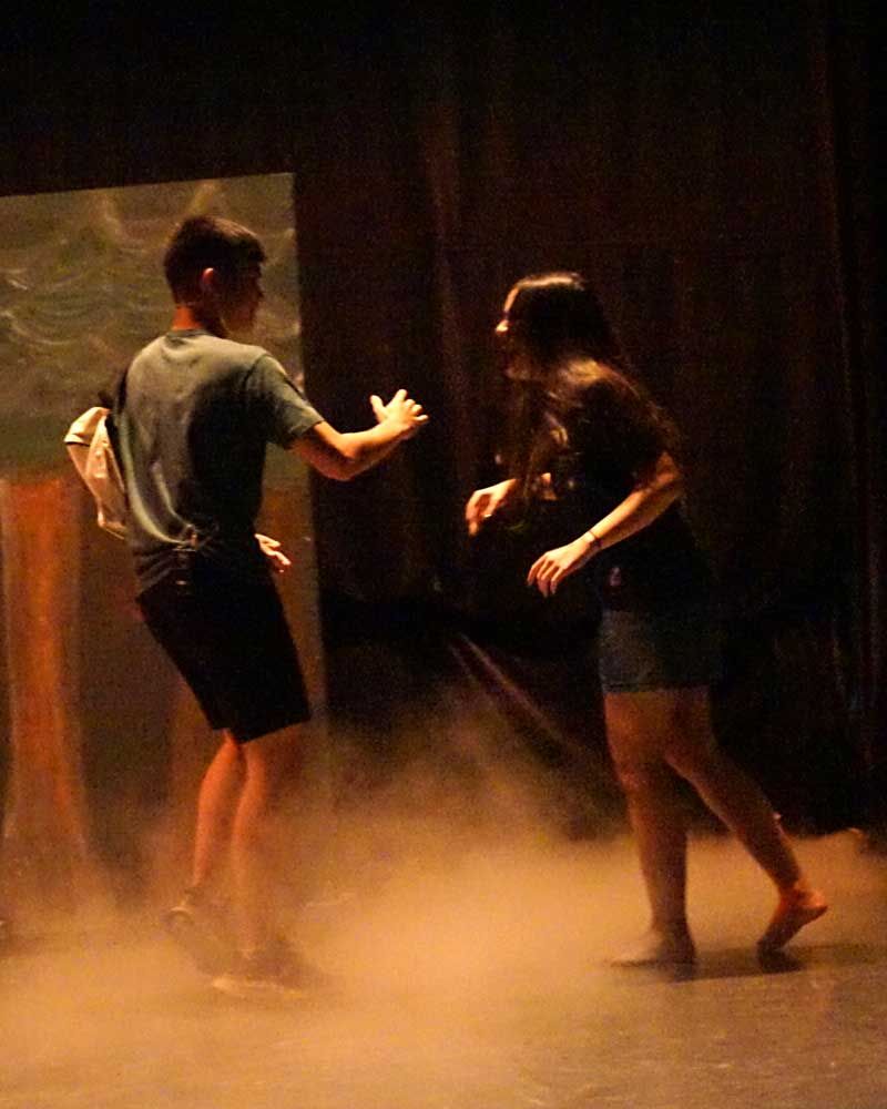 A man and a woman are dancing on a stage in a dark room.