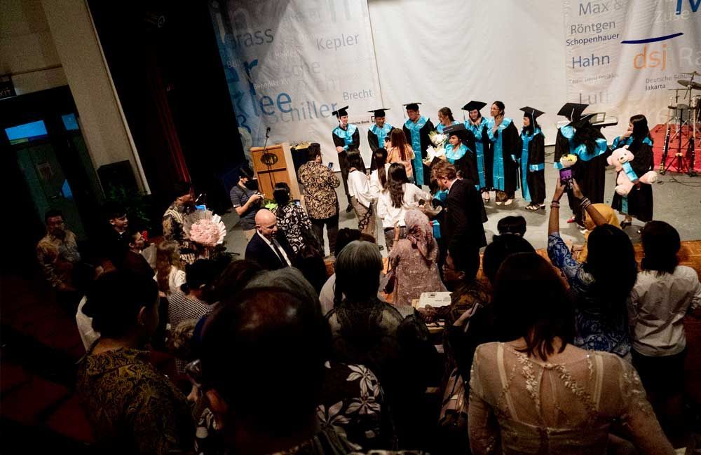 A group of people are standing in front of a stage at a graduation ceremony.