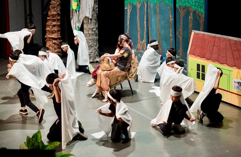 A group of people are dancing on a stage while a woman sits in a chair.