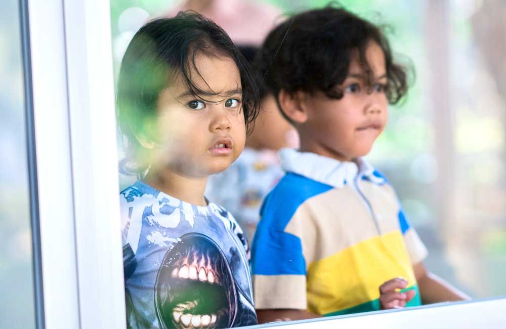 Two young children are looking out of a window.