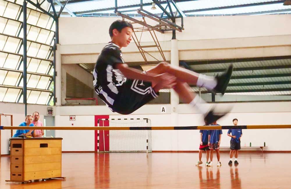A young boy is jumping over a high jump bar in a gym