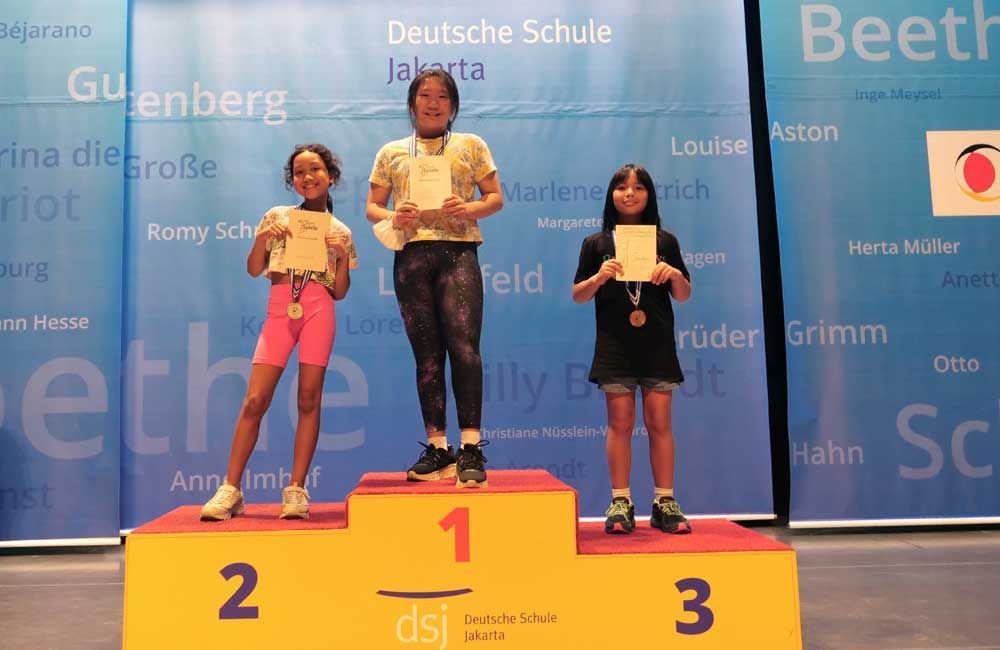 Three girls are standing on a podium with the number 1 on it