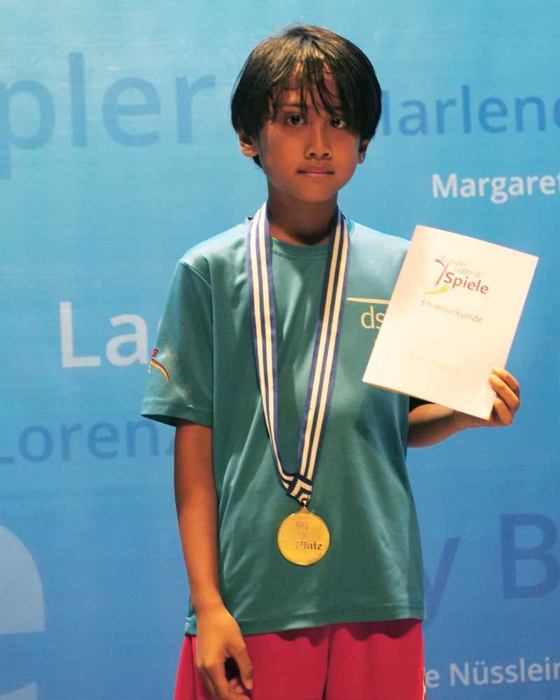 A young boy wearing a medal and holding a certificate