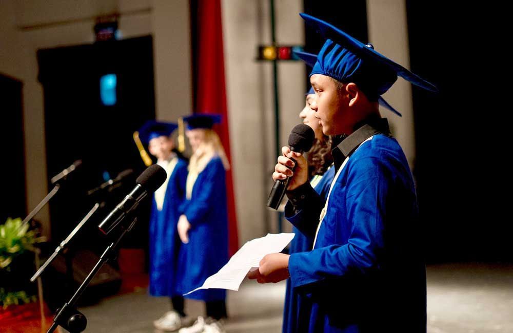 A man in a graduation cap and gown is speaking into a microphone.