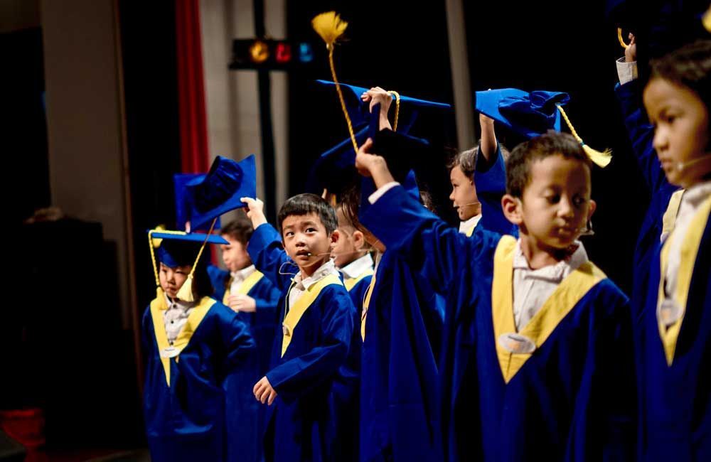 A group of children in graduation gowns and caps are standing on a stage.