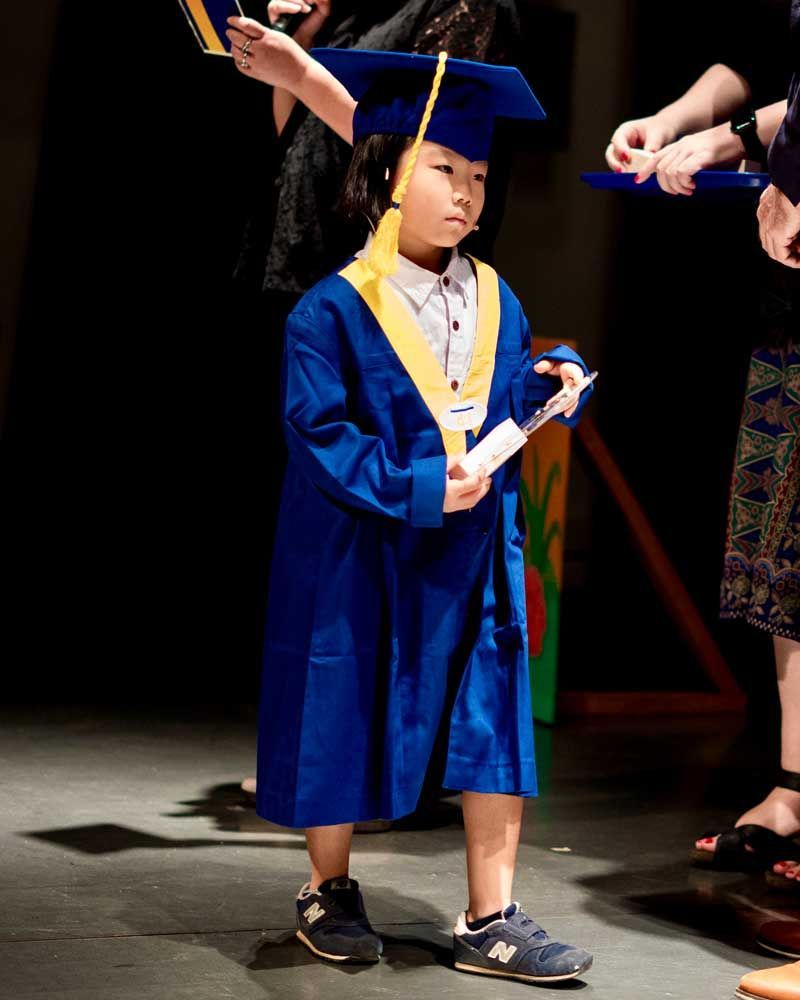 A young boy in a graduation cap and gown is holding a diploma.