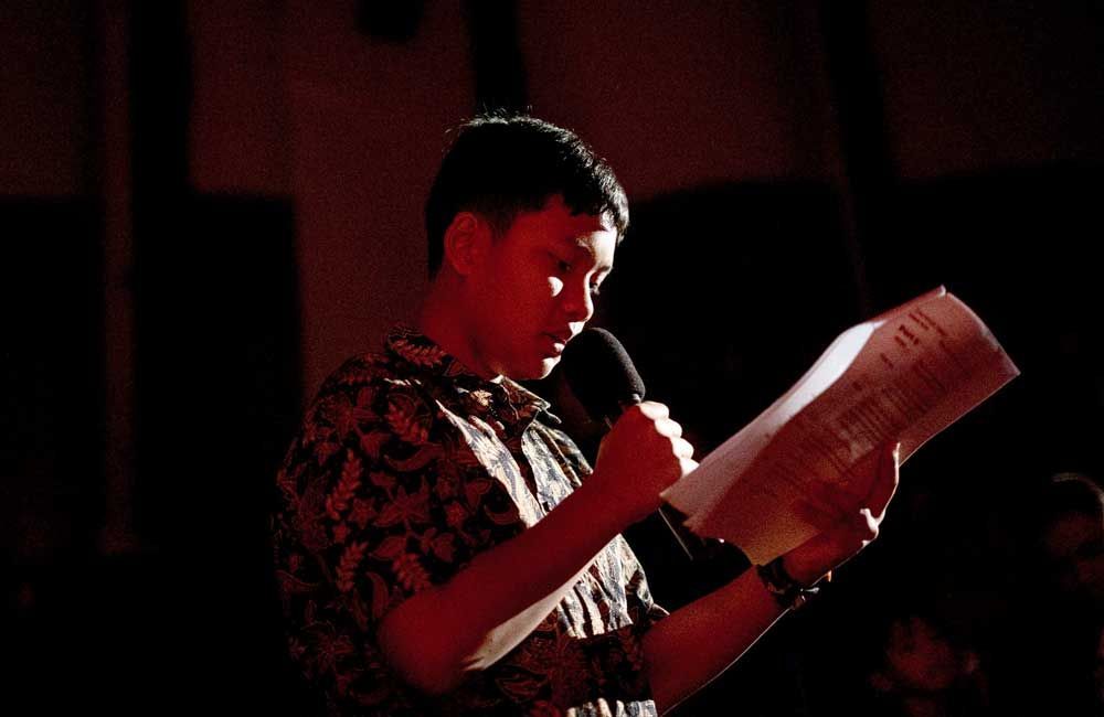 A man is holding a microphone and reading a piece of paper