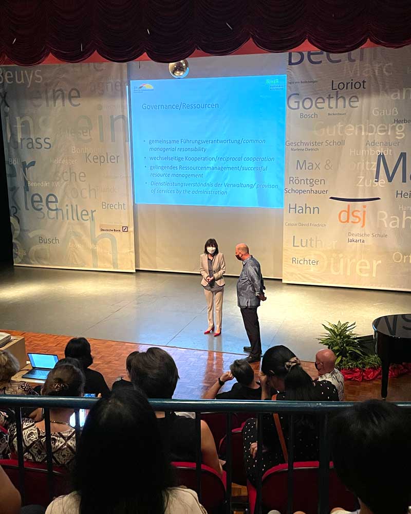 A man and a woman are standing on a stage in front of a projector screen.