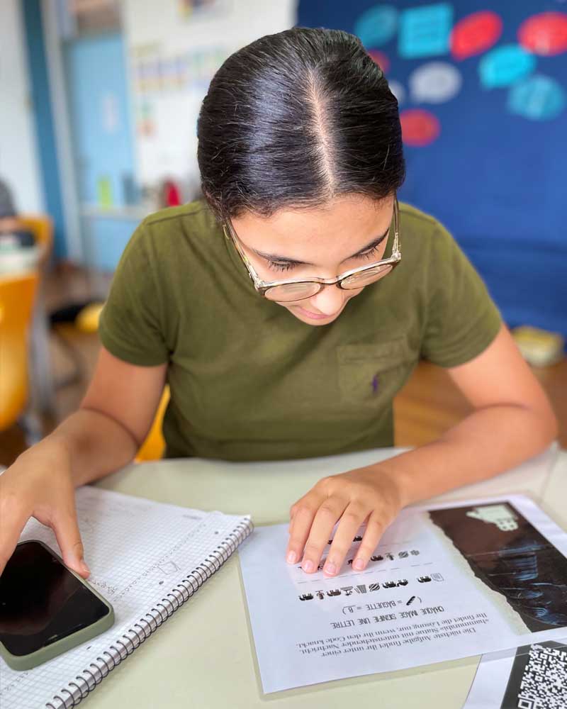 A woman is sitting at a table with a cell phone and a notebook.