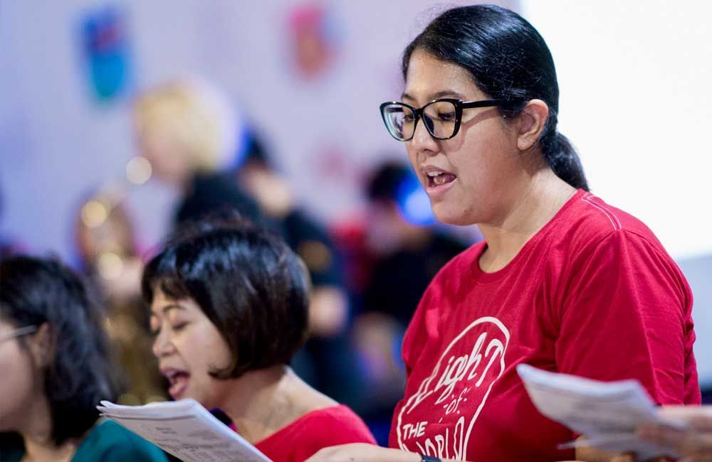 A woman in a red shirt is singing in a choir.