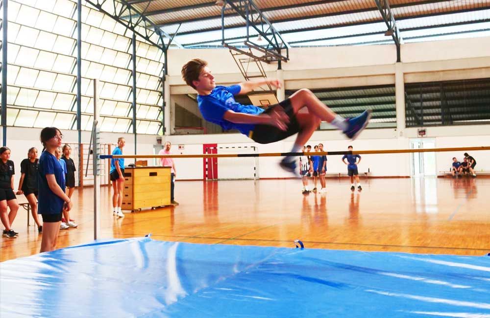 A man is jumping over a blue mat in a gym.