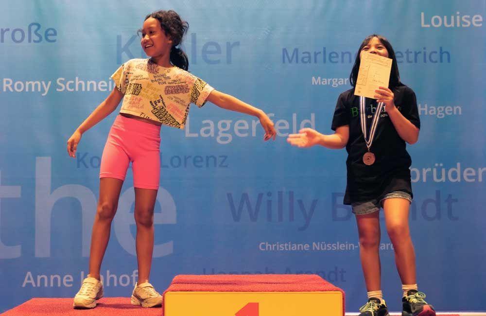 Two young girls are standing on a podium with their arms outstretched