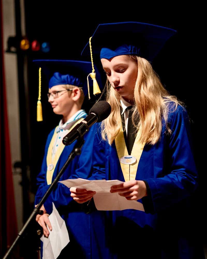 A girl in a graduation cap and gown is speaking into a microphone