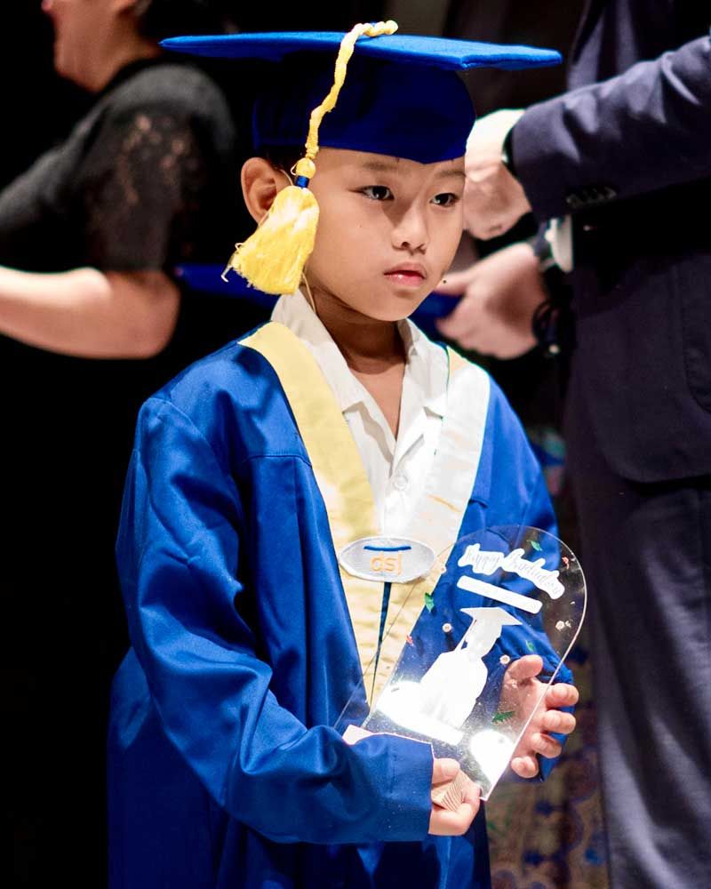 A young boy in a graduation cap and gown is holding a trophy