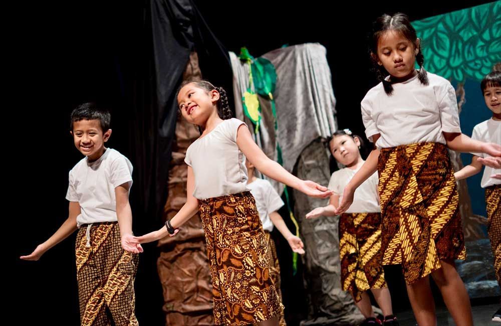 A group of children are holding hands and dancing on a stage.