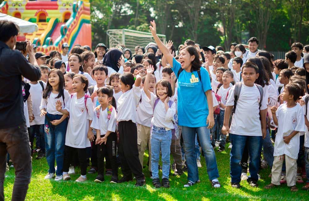 A woman in a blue shirt is standing in front of a large group of children.