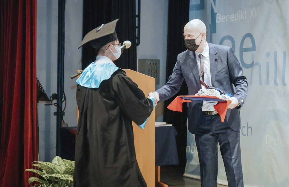 A man in a suit is shaking hands with a man in a graduation cap and gown.