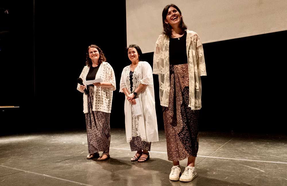 Three women are standing on a stage in front of a screen.