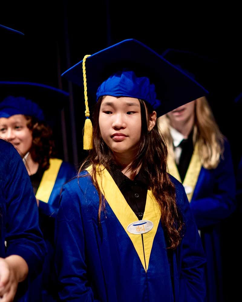 A group of graduates are standing in a line wearing blue gowns and caps.