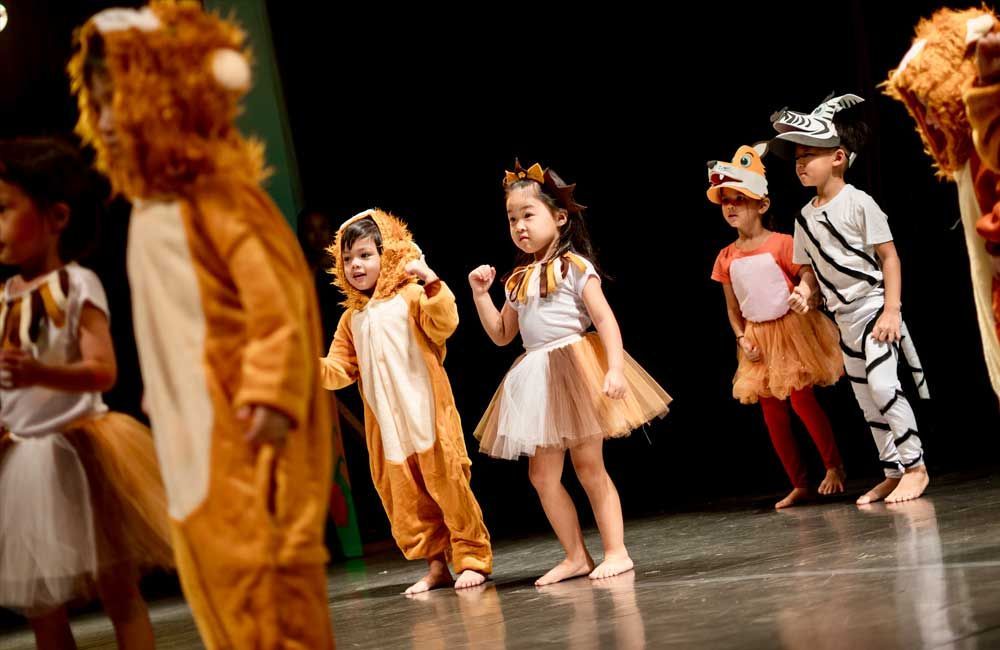 A group of children dressed in animal costumes are dancing on a stage.