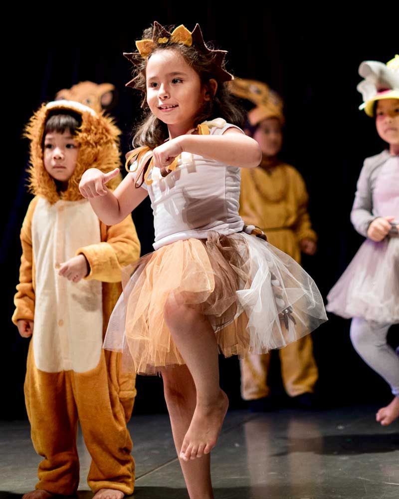 A group of children in costumes are dancing on a stage.
