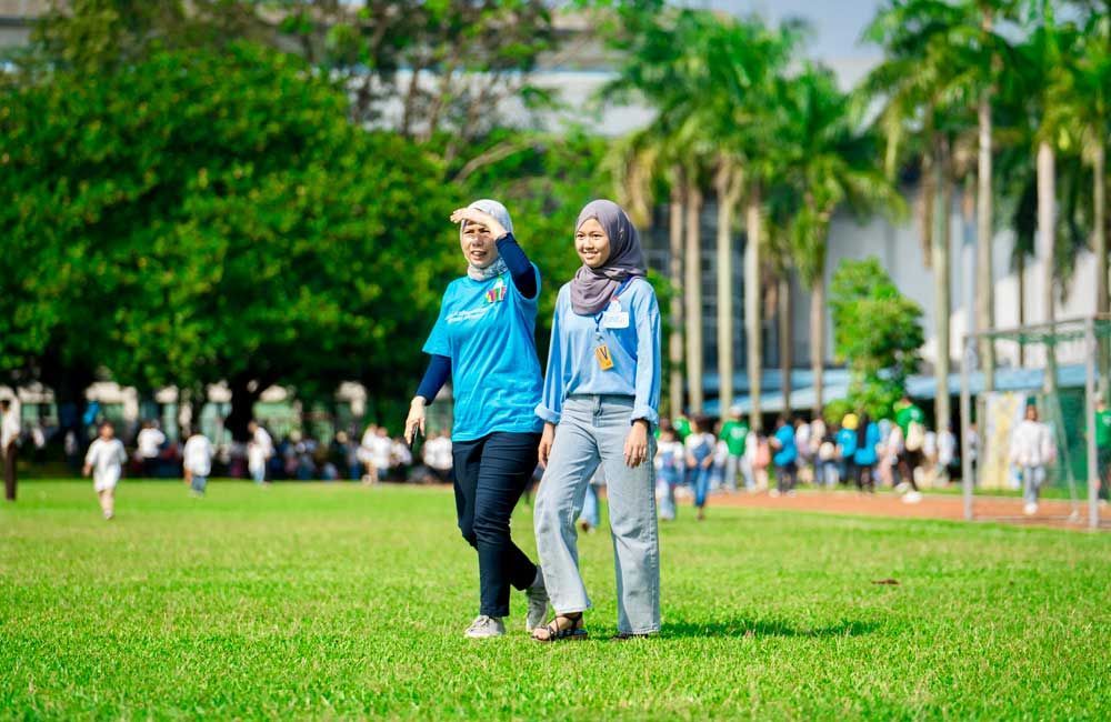 Two women are walking on a lush green field.