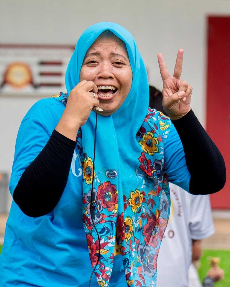 A woman wearing a blue shirt and a blue scarf is giving a peace sign