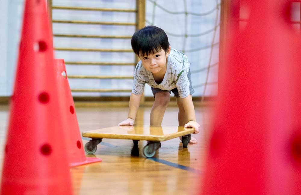 A young boy is playing with a wooden skateboard in a gym.