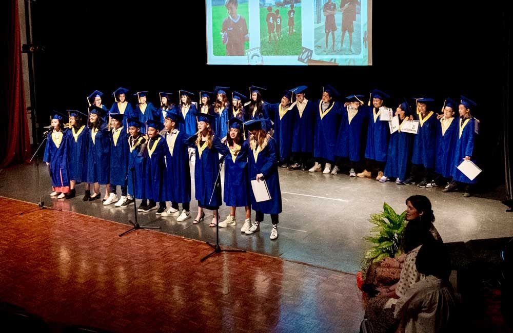 A group of children in graduation gowns are singing on a stage.