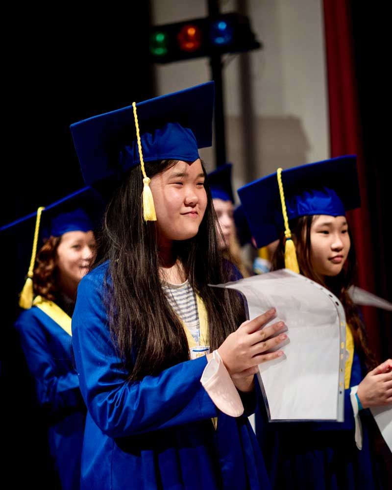 A girl in a graduation cap and gown is holding a piece of paper