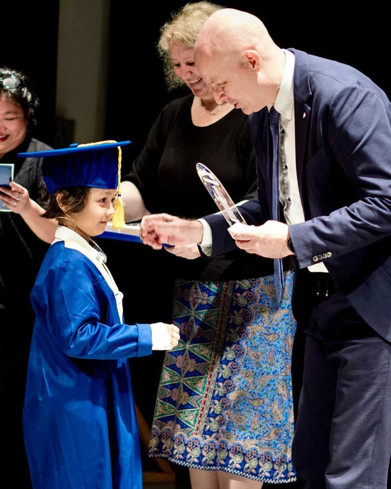 A little girl in a graduation cap and gown is being congratulated by a man in a suit