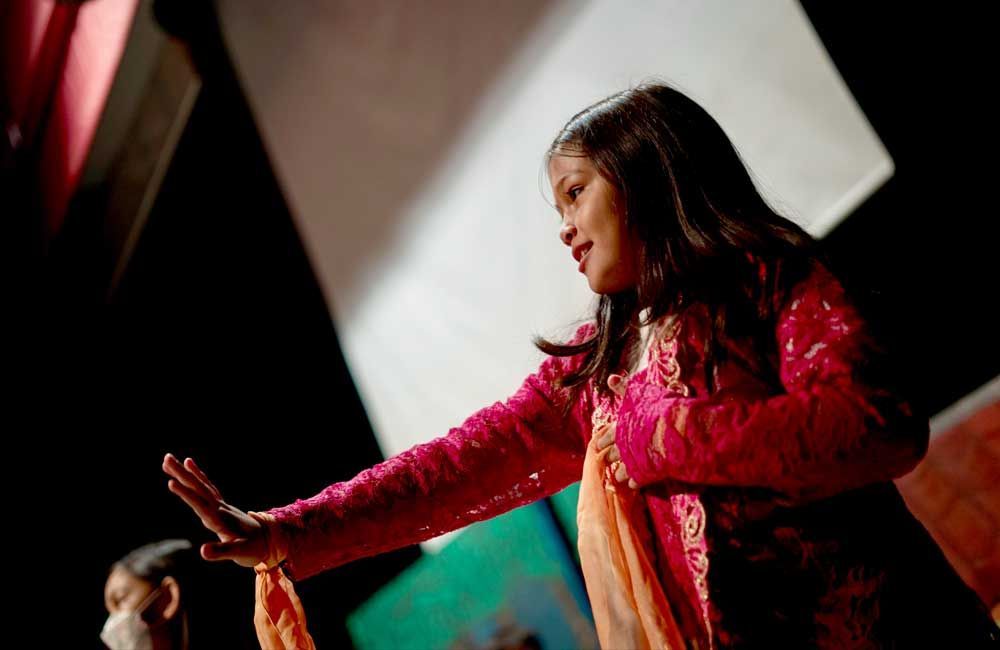 A young girl in a pink dress is dancing on a stage.