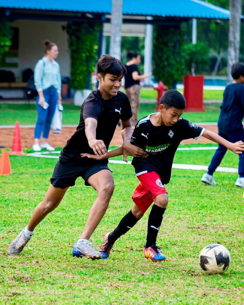 Two young boys are playing soccer on a lush green field.