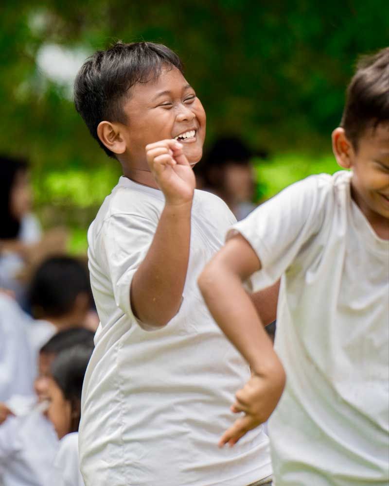 Two young boys in white shirts are standing next to each other and smiling.
