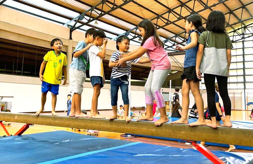 A group of children are standing on a balance beam in a gym.