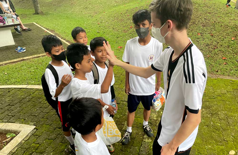 A man wearing a mask is talking to a group of children.