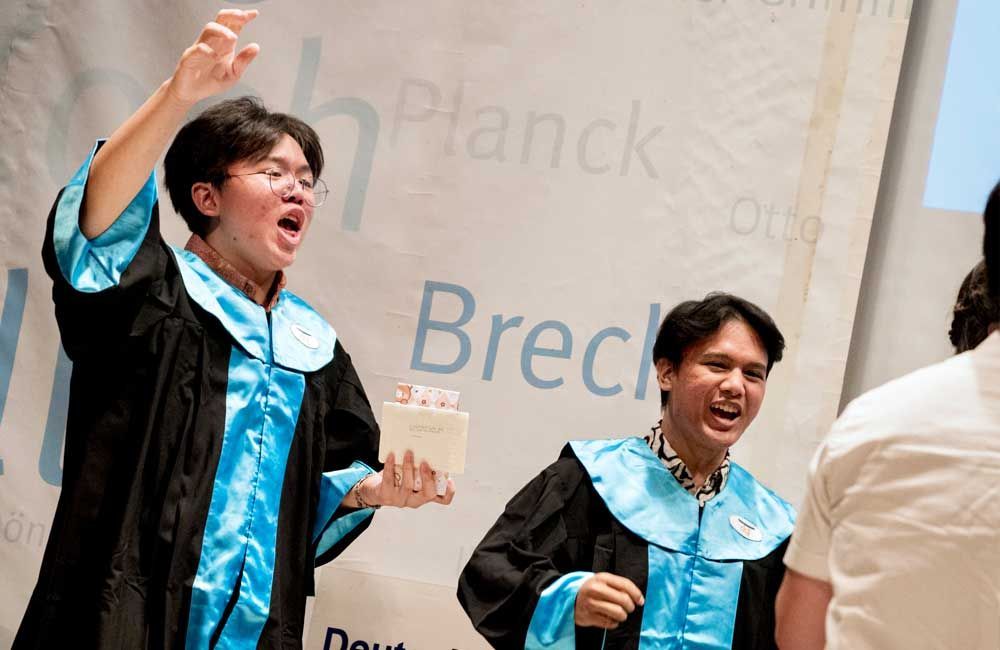 Two men in graduation gowns are standing next to each other on a stage.