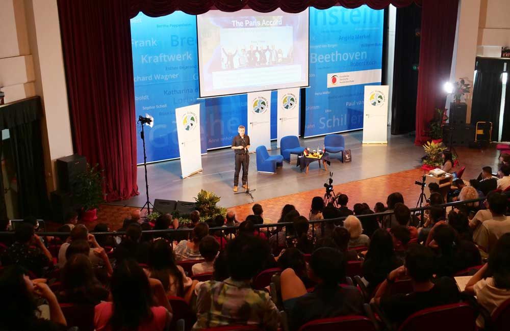 A man is standing on a stage giving a presentation to a crowd of people.