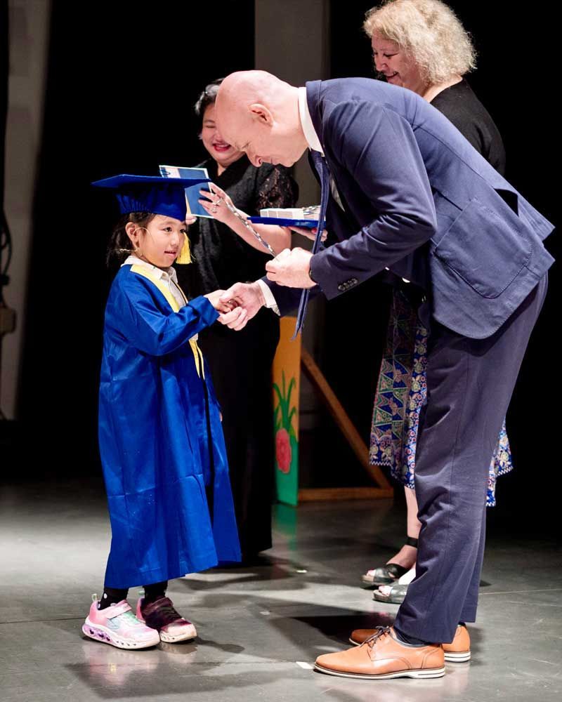 A man in a suit is shaking hands with a little girl in a graduation cap and gown