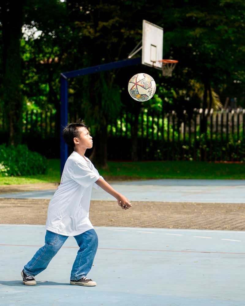 A young boy is playing with a soccer ball on a basketball court.