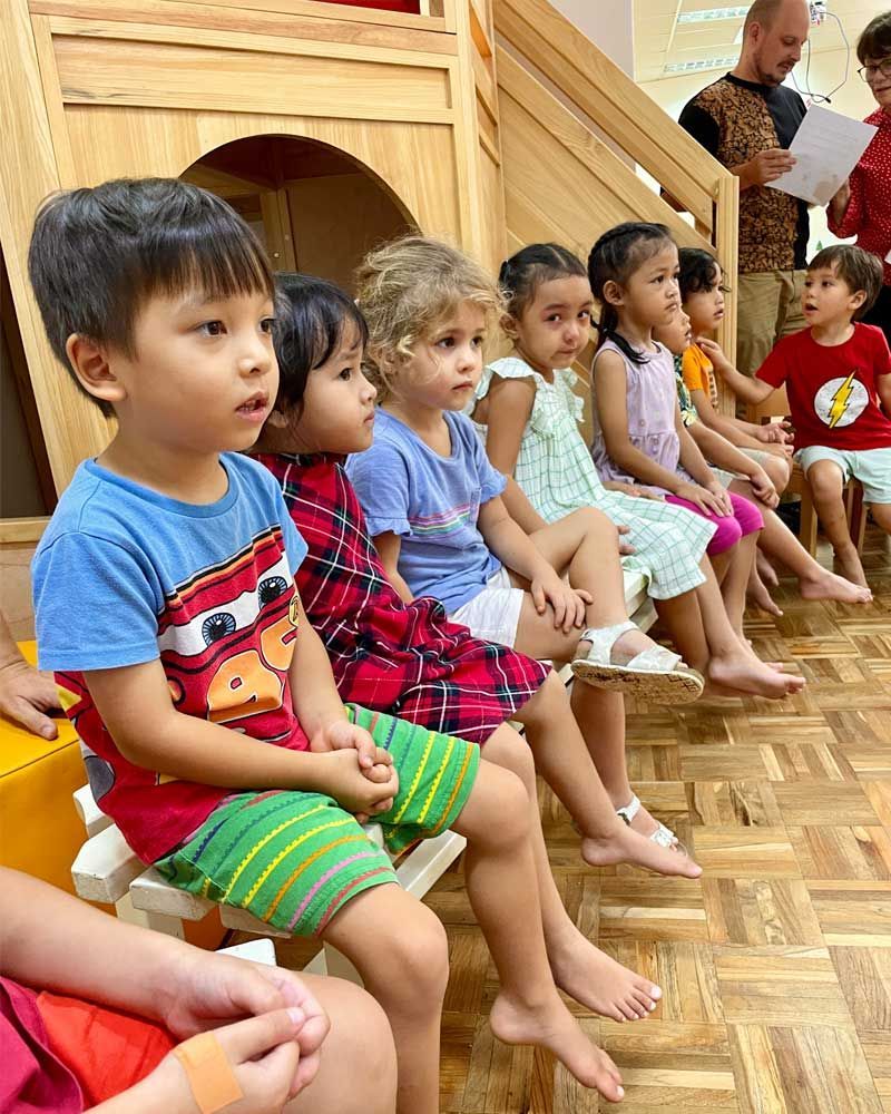 A group of children are sitting in a row on a wooden floor.