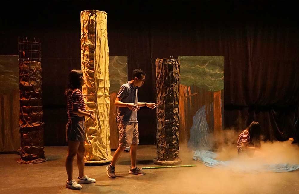 A boy and a girl are standing on a stage in front of a waterfall.