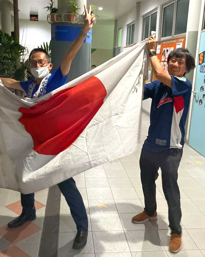 Two men are holding a japanese flag in a hallway.