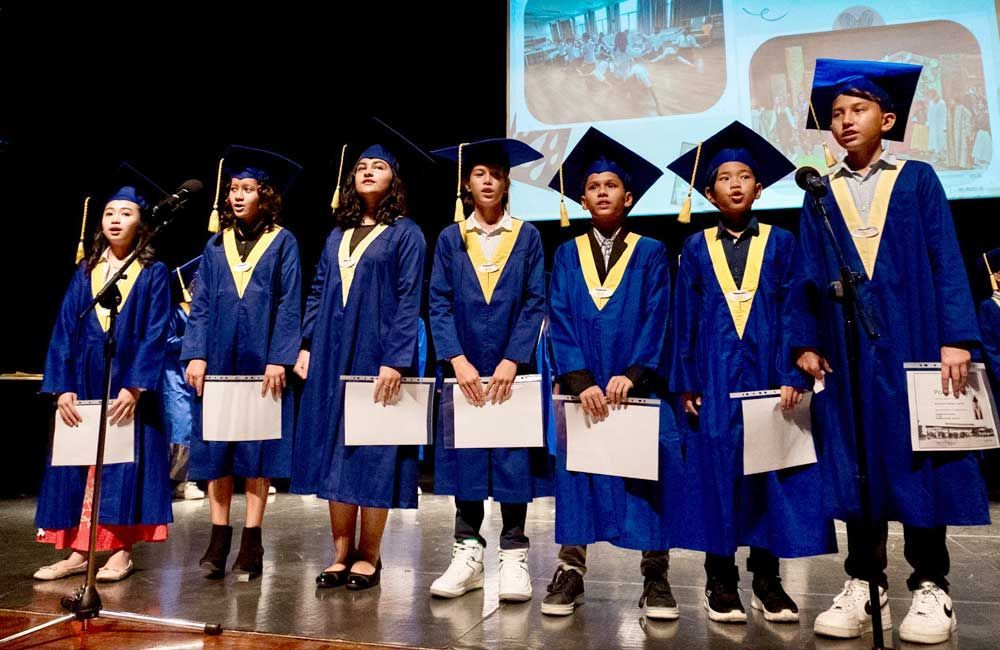 A group of children wearing graduation caps and gowns are standing on a stage.