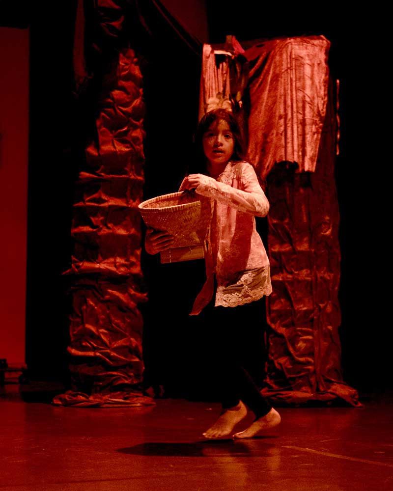 A little girl is standing on a stage holding a basket