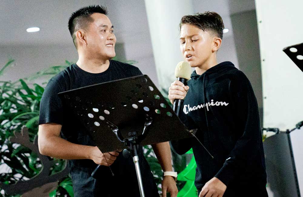 A man and a boy are singing into microphones.